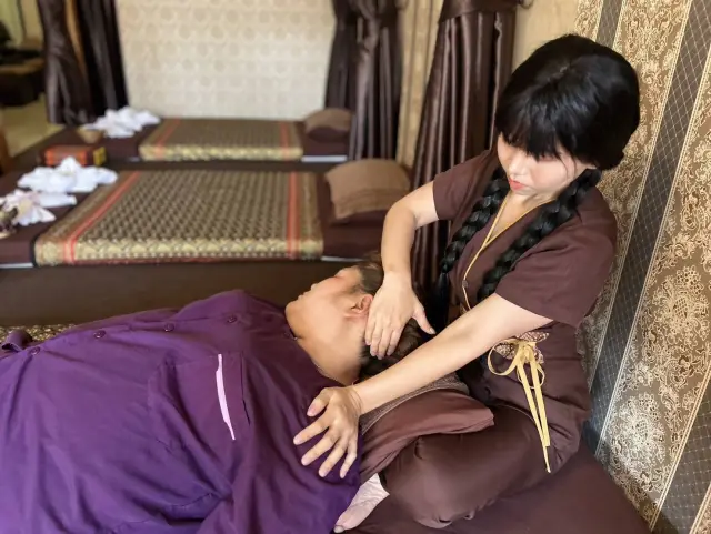 Therapist with a braid gently massaging a guest's neck and shoulders on a mat in Chiang Mai
