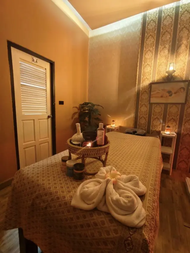 Small massage room with a bed, folded towel flower and aromatherapy tray at Ai Oon Massage Lanna