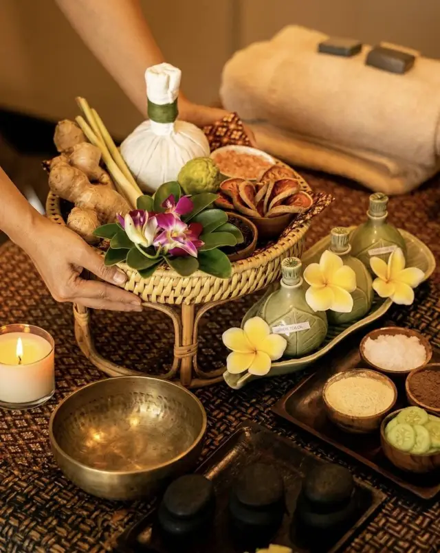 Herbal compress ball, ginger, flowers, singing bowl and basalt stones set up for a Thai massage