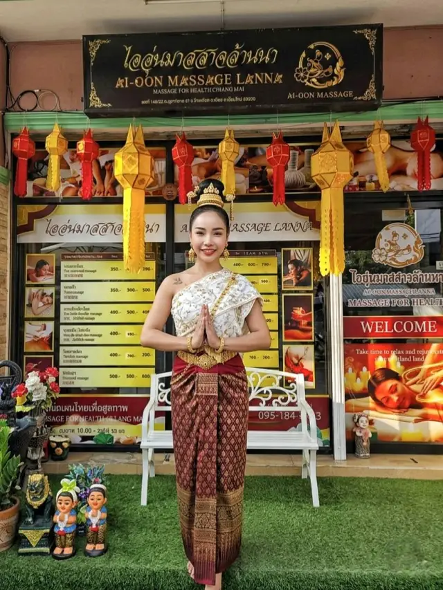 Woman in traditional Thai dress posing with a wai in front of Ai Oon Massage Lanna shop