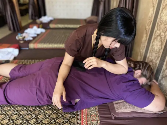 Therapist leaning over a guest in purple clothes during a Thai massage on a mat, Chiang Mai