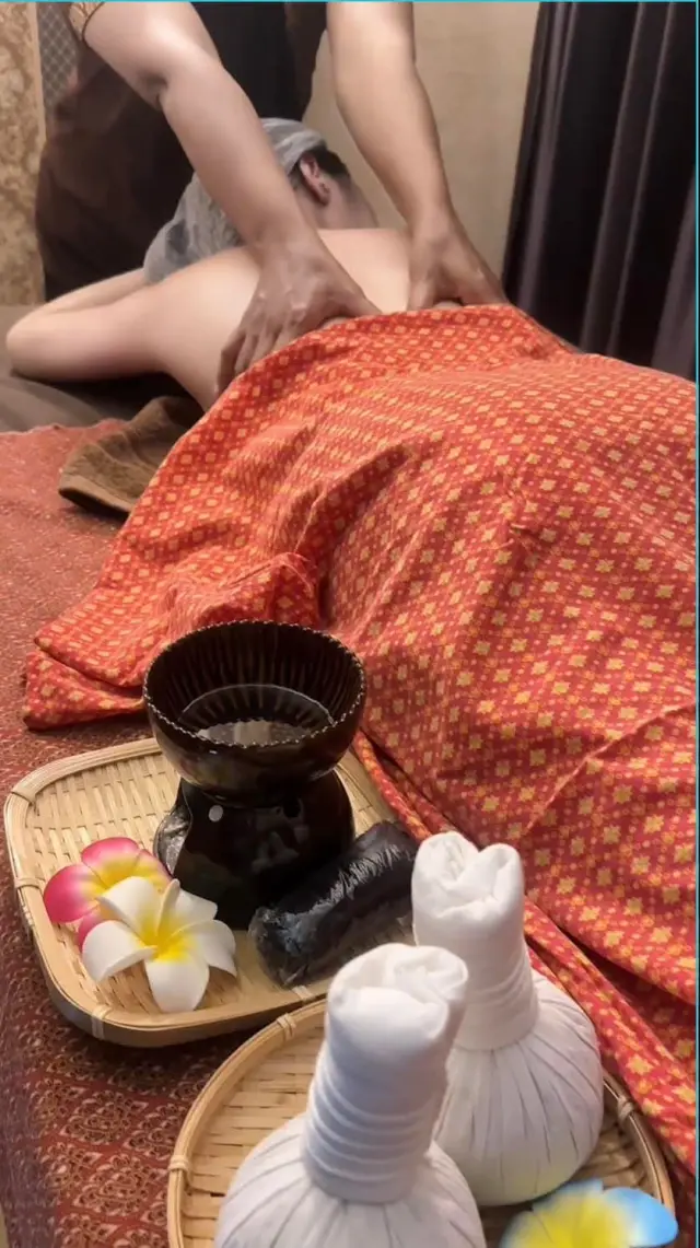 Guest lying under an orange cloth for a back massage, with herbal compress balls and a burner nearby