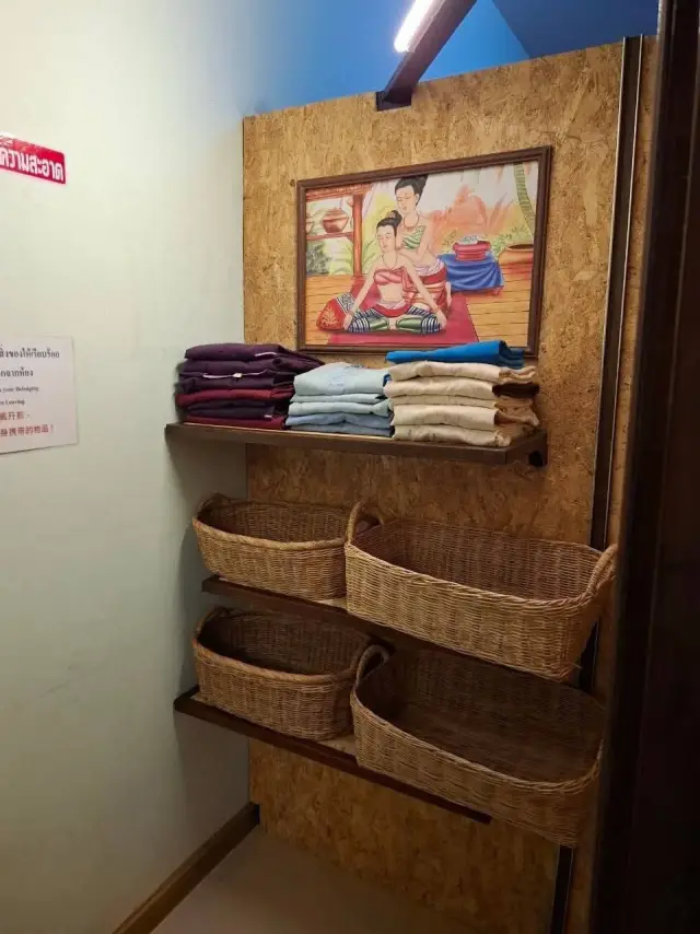 Shelves of folded towels and woven baskets beside a Thai painting at Ai Oon Massage Lanna