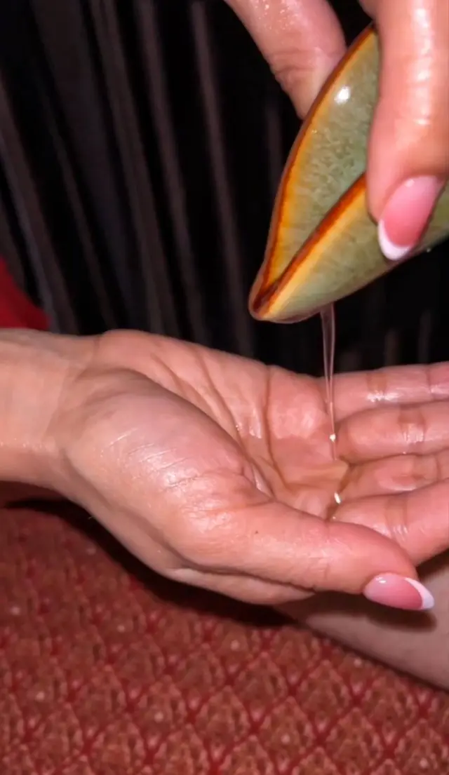 Aromatic oil being poured from a shell into a therapist's palm before a massage